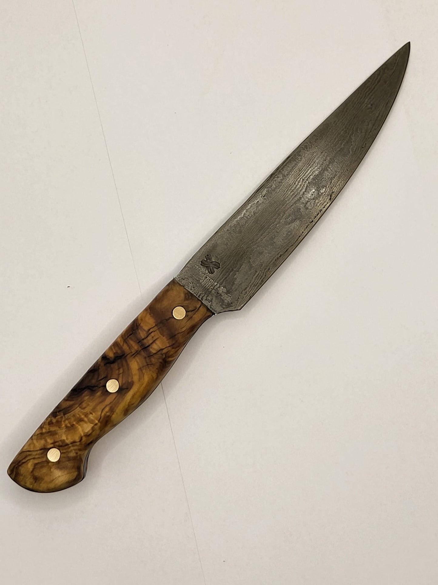 Ein hochwertiges Damastmesser mit einem eleganten Holzgriff aus Olivenholz liegt auf einer dunklen Oberfläche. Die Klinge zeigt die charakteristische wellenförmige Musterung des Damaststahls.