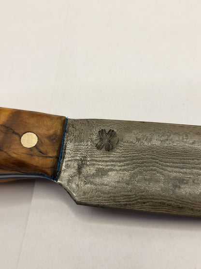 Ein Ausschnitt mit dem logo von dem Damastmesser mit einem eleganten Holzgriff aus Olivenholz liegt auf einer dunklen Oberfläche. Die Klinge zeigt die charakteristische wellenförmige Musterung des Damaststahls.
