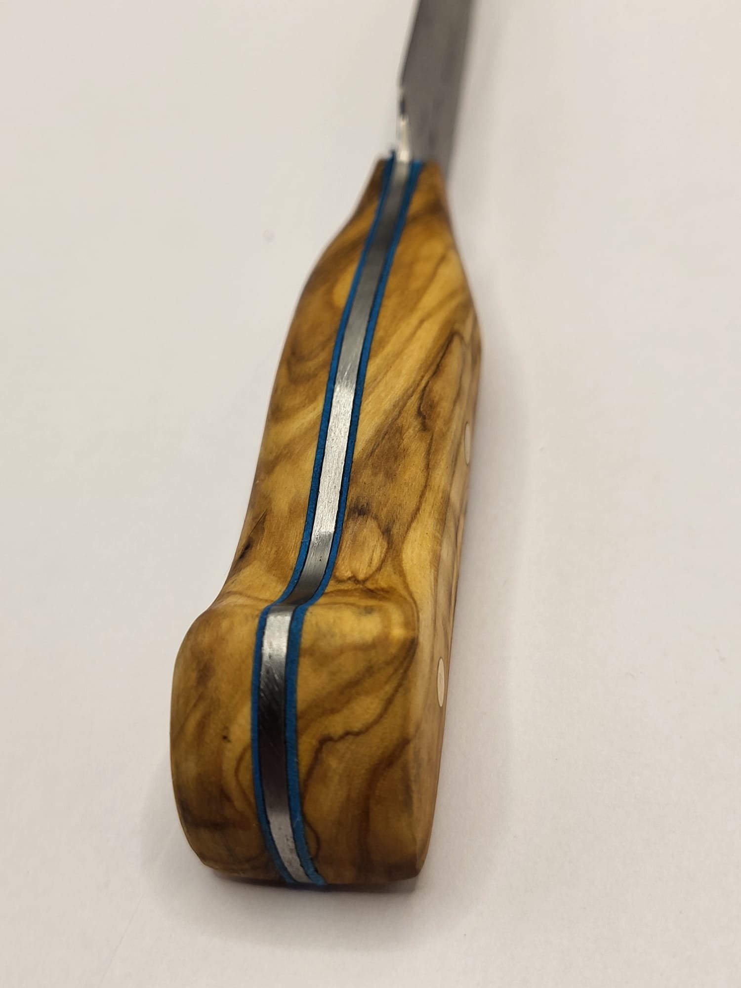 Ein hochwertiges Damastmesser mit einem eleganten Holzgriff aus Olivenholz liegt auf einer dunklen Oberfläche. Die Klinge zeigt die charakteristische wellenförmige Musterung des Damaststahls.
