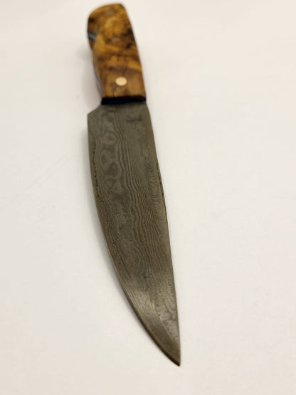 Ein hochwertiges Damastmesser mit einem eleganten Holzgriff aus Olivenholz liegt auf einer dunklen Oberfläche. Die Klinge zeigt die charakteristische wellenförmige Musterung des Damaststahls.